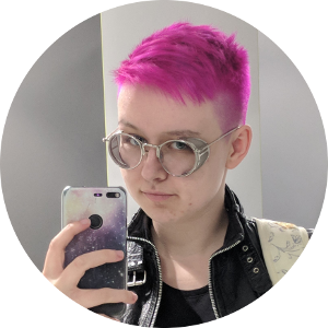 A mirror selfie of Bex with bright pink hair wearing a black leather jacket, looking at the camera, against a blank background.