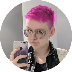 A mirror selfie of Bex with bright pink hair wearing a black leather jacket, looking at the camera, against a blank background.